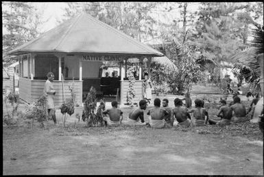 Men seated and standing around a native clinic, New Guinea, ca. 1935 / Sarah Chinnery