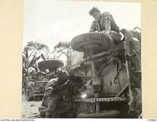 WAU, NEW GUINEA, 1944-02-20. VX104657 DRIVER F.L.F. STEVENS (1), WORKING ON THE WHEEL OF A JEEP BEING ELECTRONICALLY WELDED BY POWER SUPPLIED FROM TRUCK MACHINERY AT THE 2/34TH GENERAL TRANSPORT ..