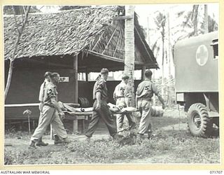LAE, NEW GUINEA, 1944-03-25. MEMBERS OF THE BUSU MEDICAL POST, 9TH FIELD AMBULANCE DETACHMENT ATTACHED TO HEADQUARTERS LAE BASE SUB-AREA, MOVE A PATIENT TO AN AMBULANCE FOR TRANSPORTATION TO ..