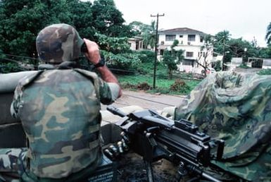 A Marine posted atop the roof of the United States Embassy sits beside a Mark 19 automatic grenade launcher as he scans the surrounding area with a pair of binoculars. Marines of the 22nd Marine Expeditionary Unit (22nd MEU), deployed aboard the amphibious assault ship USS SAIPAN (LHA 2), were sent to augment security at the embassy as part of Operation SHARP EDGE