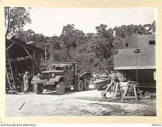 KALUMALAGI RIVER, JACQUINOT BAY, NEW BRITAIN, 1945-08-12. TROOPS AT 1 INFANTRY TROOPS WORKSHOP WORKING AT THE BEACH SLIPWAY. THE TRUCK WITH THE CRANE IS CARRYING A BOAT TO WORKSHOP FOR REPAIRS