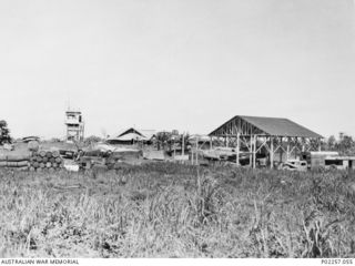 Madang, New Guinea, 1945-08. Madang Air Strip, showing buildings, aircraft, vehicles, equipment and supplies. A Bristol Beaufort aircraft of No. 15 Squadron RAAF is parked in a hangar (right). One ..