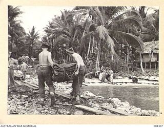 CUTARP PLANTATION, JACQUINOT BAY, NEW BRITAIN. 1944-12-15. HQ 6 INFANTRY BRIGADE TROOPS CARRYING SUPPLIES AT NAIL'S JETTY, A BEACHHEAD OF THE BRIGADE NAMED AFTER A BRIGADE OFFICER