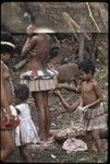 Seated woman adjusts short banana fiber skirt worn by a an adolescent girl