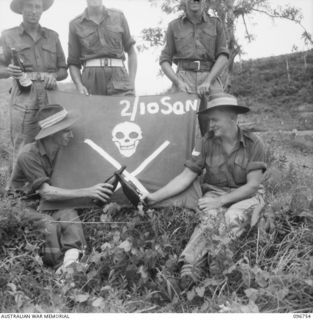 KARAWOP, NEW GUINEA, 1945-09-18. THE SKULL AND CROSS-BONE FLAG, THE PRIDE OF 2/6 CAVALRY COMMANDO REGIMENT. ON EVERY BEER ISSUE DAY THE BOYS CROSS BOTTLES BEFORE THE FLAG. IDENTIFIED PERSONNEL ..