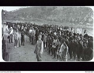 PORT MORESBY, NEW GUINEA. 1914-08. INSCRIPTION ON VERSO: "GROUP OF NATIVES AT RADIO STATION, PORT MORESBY, AUG 1914, RECEIVING INSTRUCTIONS". A LARGE CROWD OF NATIVES ARE GATHERED, A SERGEANT OF ..