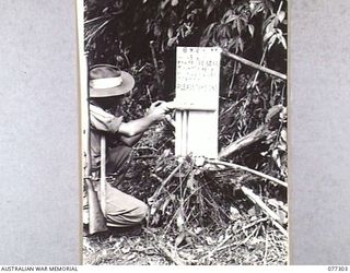 TOROKINA AREA, BOUGAINVILLE ISLAND. 1944-11-28. QX37937 SERGEANT D.L. BIRKBECK , 9TH INFANTRY BATTALION, PLACING A BUNDLE OF LEAFLETS IN A HOLDER ON A NOTICE BOARD ERECTED BY AN AUSTRALIAN PATROL ..