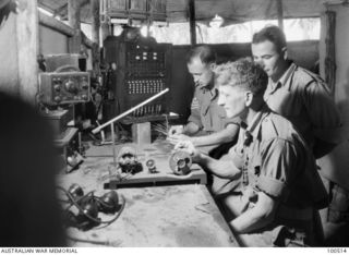 Lae, New Guinea. 1944-06-18. Members of 17 Technical Maintenance Section working on the repair of a thirty-line wall type PMG switchboard. Left to right: Staff Sergeant J. W. Harvey; Signalman C. ..