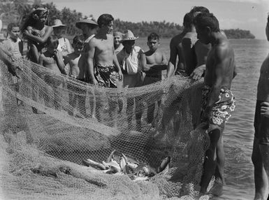 [Group of Pacific Island people on beach examining fishing nets]