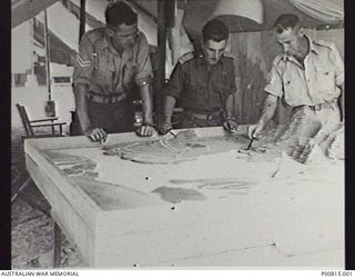 BOUGAINVILLE, 1944. HEADQUARTERS 2 AUSTRALIAN CORPS. LEFT TO RIGHT: CORPORAL PAT FLYNN, LIEUTENANT FRANK KING AND ARTHUR PITTS LOOKING AT A TERRAIN RELIEF MODEL. (DONOR A. BARING)