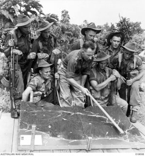 Aitape, New Guinea. 1944. An Australian section patrol about to leave a forward area headquarters bound for Japanese held jungle being briefed on terrain by an Intelligence Officer. Models are made ..