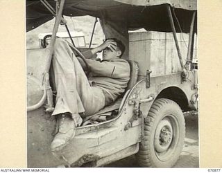 WAU - BULLDOG ROAD, NEW GUINEA, 1944-02-24. NX151673 DRIVER R.T. KENNEDY (1), OF THE 2/34TH GENERAL TRANSPORT COMPANY, RELAXING WHILE THE CONVOY UNLOADS. THE STRAIN OF DRIVING OVER THE ROAD IS ..