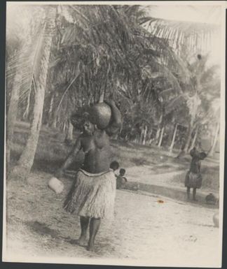 Woman wearing a grass skirt and carrying a pot on her shoulder, Port Moresby, Papua, ca. 1923 / Sarah Chinnery