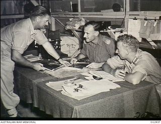 TOROKINA, BOUGAINVILLE ISLAND, SOLOMON ISLANDS. 1945-04-11. IN THE OFFICE, ARMY AND RAAF PERSONNEL EXAMINING PHOTOGRAPHS TAKEN DURING A PHOTO RECONNAISSANCE MISSION OVER JAPANESE-HELD TERRITORY ON ..