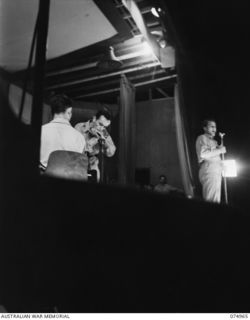 LAE, NEW GUINEA. 1944-07-24. LARRY ADLER, THE WORLD'S FAMOUS AMERICAN HARMONICA PLAYER (1) PROVIDES THE MUSIC WHILE LIEUTENANT ARCHIE JONES, UNITED STATES ARMY (2) RENDERS A SONG DURING A SHOW ..