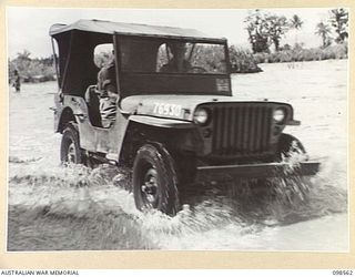 LAE, NEW GUINEA. 1945-10-14. JEEP OF FIRST ARMY MOVING ALONG THE FLOODED ROADWAY TO CROSS THE BUTIBUM BRIDGE. FOLLOWING HEAVY RAINS THE BUTIBUM RIVER OVERFLOWED ITS BANKS, FLOODED THE ROAD AND ..