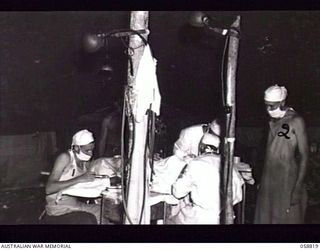 DUMPU, NEW GUINEA. 1943-10-15. AN OPERATION IN PROGRESS IN THE OPERATING THEATRE AT THE 2/6TH AUSTRALIAN FIELD AMBULANCE. A JEEP MOROR VEHICLE HEADLAMPS WERE USED AS IMPROVISED FLOODLIGHTS. SHOWN ..