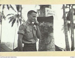 QX44994 Corporal Leonard Arthur Mobsby, a member of Headquarters, 5th Division using the public telephone installed in the camp