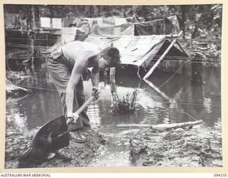 SOUTH BOUGAINVILLE. 1945-07-21. PRIVATE K.G. KIRK, 58/59 INFANTRY BATTALION, DIGGING A DRAIN IN AN ATTEMPT TO DRAIN FLOOD WATER FROM HIS TENT. THE 20-INCH RAINFALL IN THE LAST THREE WEEKS HAS ..