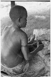 Woman wearing a cross, cooking and scraping taro on fire at Ngarinaasuru, above Sinalagu