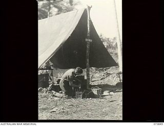 Madang, New Guinea. 1944-06-14. QX53075 Craftsman H. J. Nasser, electrician at 266th Light Aid Detachment, Headquarters 15th Infantry Brigade, tests batteries outside the tent workshop. The unit is ..