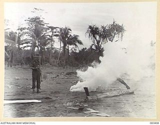 BABIANG AREA, NEW GUINEA, 1944-11-19. A MEMBER OF 2/10 COMMANDO SQUADRON EXAMINES A FLARE. THE SMOKE GIVES WIND DIRECTION AND SPEED APPROXIMATION TO A BEAUFORT BOMBER PILOT OF 100 SQUADRON, RAAF, ..