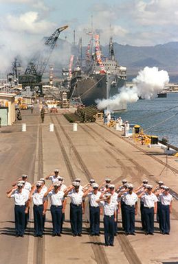 A Coast Guard honor guard salutes and howitzers are fired during the designation and departure ceremony for the Unknown Serviceman of the Vietnam Era. At the conclusion of the ceremony, the Unknown will be placed aboard the frigate USS BREWTON (FF 1086) and transported to Naval Air Station Alameda, California. The repair ship USS JASON (AR 8) is visible in the background