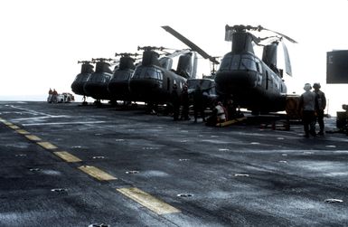 Several CH-46 Sea Knight helicopters on the flight deck of the amphibious assault ship USS GUAM (LPH 9) during Operation URGENT FURY off the coast of Grenada. A UH-1 Iroquois helicopter is parked between two Sea Knights