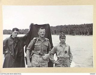 BUKA PASSAGE, BOUGAINVILLE AREA. 1945-09-16. LIEUTENANT R.N. KEAM, ARMY PHOTOGRAPHER, HEADQUARTERS 2 CORPS, STANDING ON THE REAR OF A BARGE WITH AUSTRALIAN SOLDIER AND JAPANESE NAVAL OFFICER DURING ..