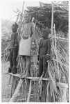 Folofo'u, wearing old police belt, on speaking platform with fernwood 'ea figures made by Arimae of Furi'ilae for the opening of the Kwaio Cultural Centre in August 1979