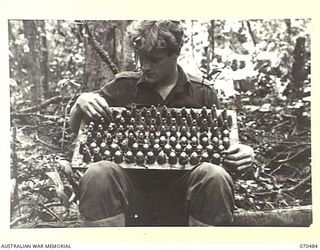 KANKIRYO SADDLE, FINISTERRE RANGE, NEW GUINEA, 1944-02-09. VX113419 PRIVATE F.H. HENDERSON, 2/9TH INFANTRY BATTALION AT A CAPTURED JAPANESE DUMP ON THE KANKIRYO SADDLE. HE IS HOLDING A TRAY OF HIGH ..