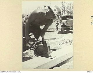 BOUGAINVILLE ISLAND, 1945-01-19. N51443 SAPPER A. SELLARS, 5TH FIELD COMPANY, USING A PORTABLE CIRCULAR SAW TO CUT BRIDGE PLANKING TO LENGTH ON THE NEW BRIDGE THE UNIT IS BUILDING ACROSS THE REINI ..