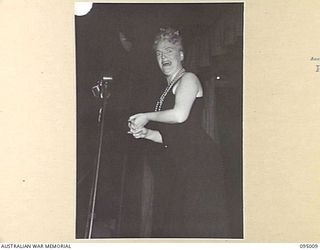 LAE AREA, NEW GUINEA. 1945-08-18. GRACIE FIELDS PRESENTING A NUMBER DURING HER CONCERT AT THE LAE BASE THEATRE