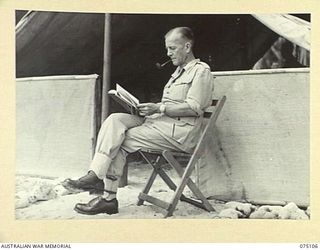 MILILAT, NEW GUINEA. 1944-08-07. QX35567 MAJOR A.G. ROWELL, DEPUTY ASSISTANT ADJUTANT GENERAL, HEADQUARTERS, 5TH DIVISION, ENJOYING A QUITE READ OUTSIDE HIS TENT