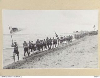 TOROKINA, BOUGAINVILLE, 1945-07-08. THE SOLOMON ISLAND SURF LIFE SAVING CLUB, FOLLOWED BY THE TEAM REPRESENTING ROYAL AUSTRALIAN NAVY, TAKING PART IN THE MARCH PAST DURING THE CHAMPIONSHIP SURF ..