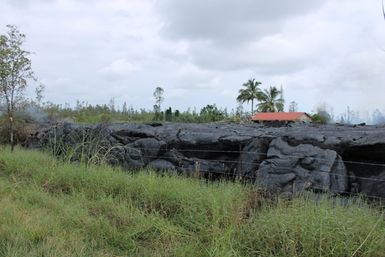 Side view of cooled lava wall near barbed wire fence, a result of Kilauea Volcano eruption and lava flow in 2014.