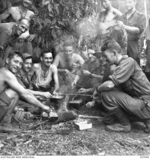 PAPUA, NEW GUINEA. 1942-10. SOLDIERS OF THE 2/31ST AUSTRALIAN INFANTRY BATTALION HEAT UP THEIR FRUGAL MEAL OF BULLY BEEF AND BISCUITS ALONG THE TRACK OVER THE OWEN STANLEY RANGES NEAR MENARI