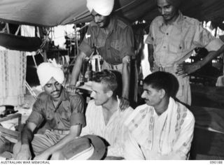 AITAPE, NEW GUINEA. 1945-03-29. INDIAN TROOPS EXAMINE WITH INTEREST AN AUSTRALIAN SLOUCH HAT HELD BY CORPORAL J. MALONEY, 2/4 INFANTRY BATTALION DURING THEIR RECUPERATION AT 104 CASUALTY CLEARING ..