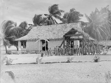 [Group portrait of young students standing outside school building]