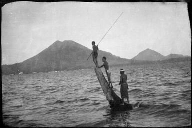 Three people standing on a tree stump in the water with the Mother Mountain beyond, Rabaul Harbour, New Guinea, ca. 1929 / Sarah Chinnery