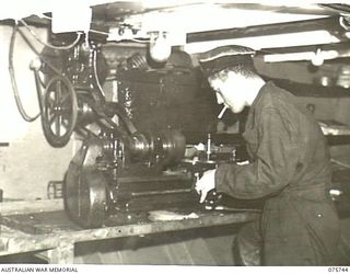 AT SEA. 1944-08/09. AN ENGINE ROOM ARTIFICER OPERATING A SMALL LATHE ABOARD THE RAN CORVETTE, GEELONG AS THE VESSEL PROCEEDS ALONG THE COAST OF NEW GUINEA