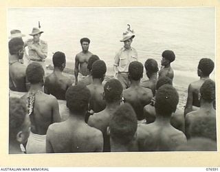 HOSKINS, NEW BRITAIN. 1944-10-13. NGX360 SERGEANT T.A. KEENAN, AUSTRALIAN NEW GUINEA ADMINISTRATIVE UNIT WITH HIS "BOSS BOYS", MO AND MUNDAI GIVING INSTRUCTIONS TO THE NATIVES FOR THEIR DAYS WORK ..