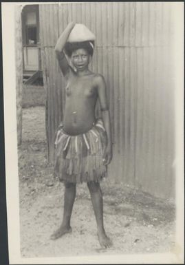 Young girl wearing a grass skirt with a parcel of sago on her head, Awar, Sepik River, New Guinea, 1935 / Sarah Chinnery