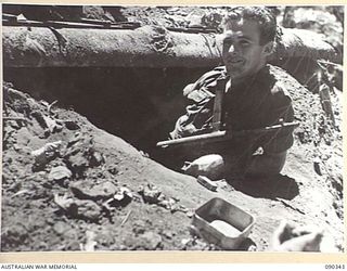 Pte James Stanley (Jim) Perejuan of Geraldton, WA, resting on the edge of his dugout on Slater's Knoll after the failure of a fierce Japanese counter attack against Battalion HQ and B Company, 25 ..