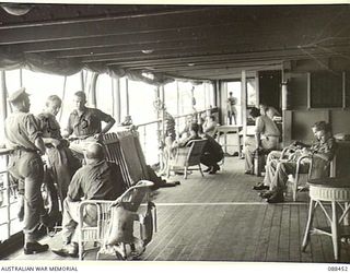 FINSCHHAFEN, NEW GUINEA. 1945-04-04. THE PORT PROMENADE DECK OF THE VAN HEUTSZ SHOWING OFFICERS AT EASE IN THE FOREGROUND AND DREGER BAY IN THE BACKGROUND AS THE VESSEL, CARRYING HEADQUARTERS 26 ..