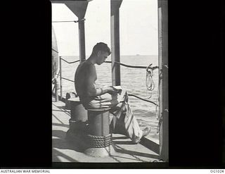 AT SEA EN ROUTE TO AITAPE, NORTH EAST NEW GUINEA. 1944-04-20. LEADING AIRCRAFTMAN G. JATSEAS OF INVERELL, NSW, HAS A QUIET READ ON DECK DURING THE TRIP WHICH WAS AS GOOD AS A PEACE TIME TROPICAL ..