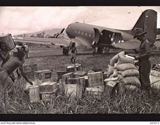 NADZAB AIRSTRIP, NEW GUINEA. 1943-09-18. NATIVES UNLOADING SUPPLIES FROM AIRCRAFT. ON THE RETURN JOURNEY WOUNDED SOLDIERS WILL BE FLOWN BACK TO BASE HOSPITALS