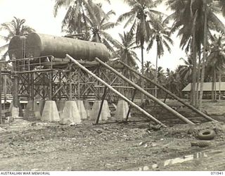 MILNE BAY, PAPUA, NEW GUINEA. 1944-04-03. TWO 12,000 GALLON STORAGE TANKS OPERATING AT THE 2ND BULK PETROLEUM STORAGE COMPANY. THE SKIDS ARE POSITIONED TO ROLL A THIRD TANK OF THE SAME CAPACITY TO ..