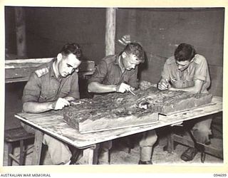 YALU, NEW GUINEA. 1945-08-03. LIEUTENANT J.L. DAVIES (1), PRIVATE J.E. JORDAN (2), AND CORPORAL R.C. EVANS (3), MAKING A MASTER MODEL WITH PLASTICINE. THE MEN ARE STUDENTS AT THE NEW GUINEA ..