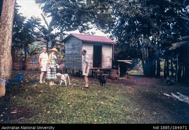 Three people and two dogs in front of shed